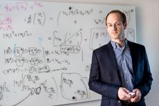 Andrew Childs stands in front of a white board with equations.