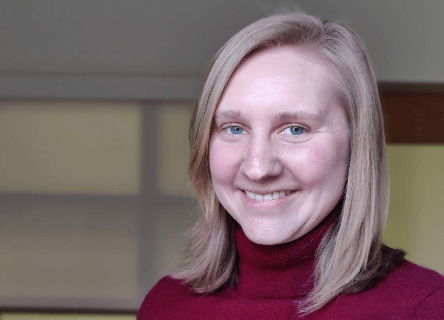 a woman smiling at the camera and wearing a red turtleneck