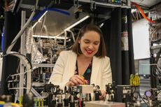 Crystal Noel smiles while adjusting complex laser equipment and optical components in a quantum engineering laboratory.