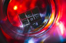 A square microchip with etched circuits illuminated inside a glass container with vibrant red and golden reflections.